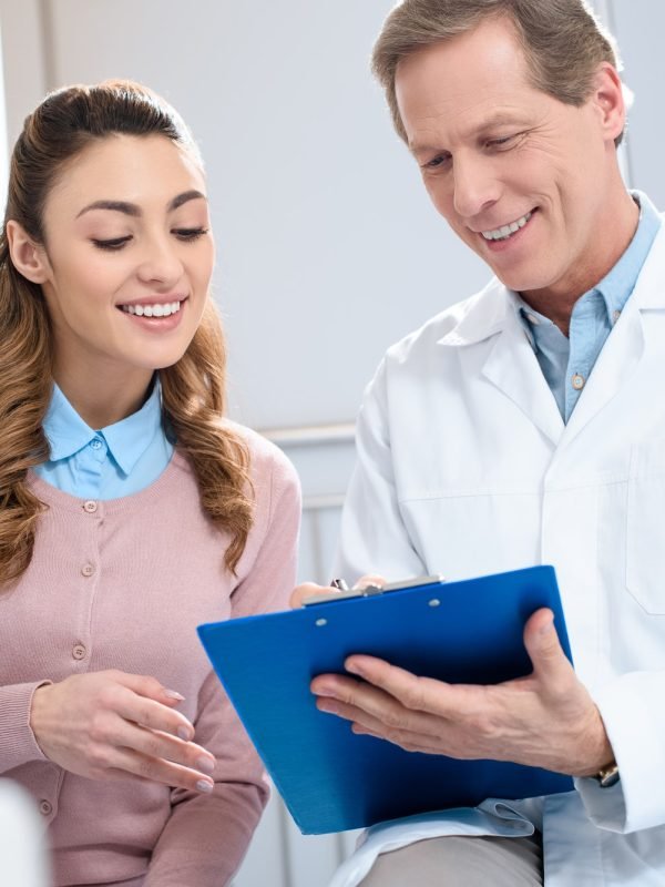 handsome-doctor-showing-something-in-clipboard-to-smiling-patient-in-clinic.jpg
